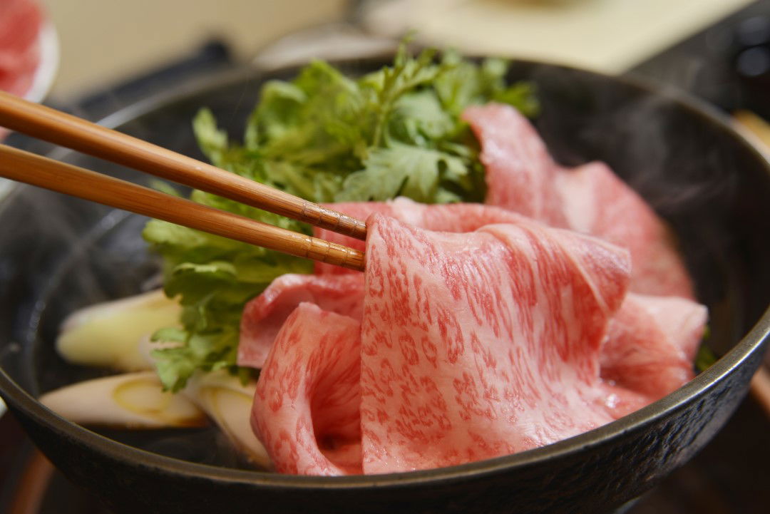 Japanese Wagyu beef in hot pot with chopsticks and fresh greens