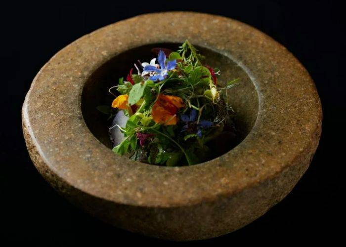 A picturesque serving at Hommage, featuring a flower-decorated salad in a thick, stone bowl.