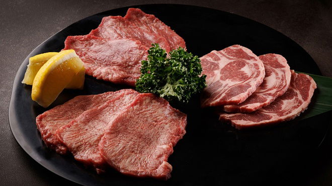 Multiple slices of wagyu beef at Yakiniku Horumon Tasuki Akasaka, served with slices of lemon and herbs.