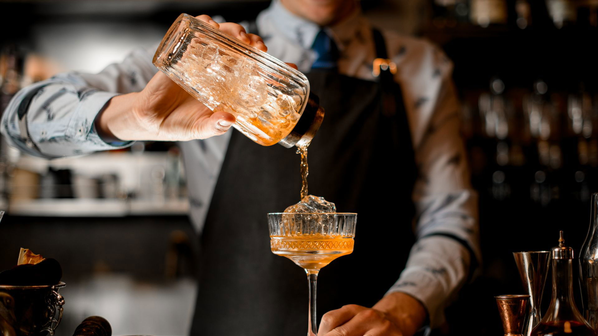 Bartender expertly pours cocktail into a glass on bar counter