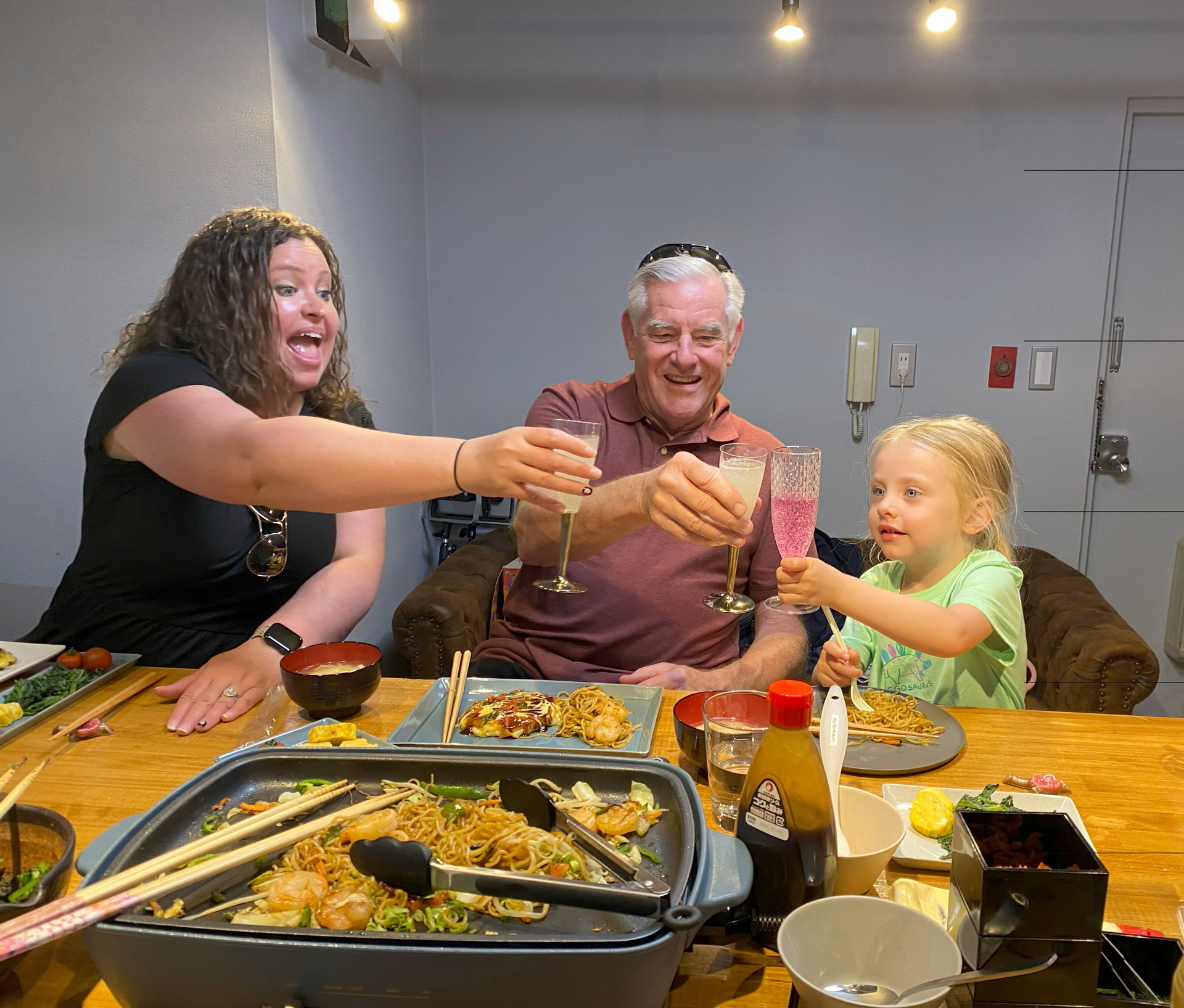 A family clinking glasses while enjoying freshly made yakisoba.