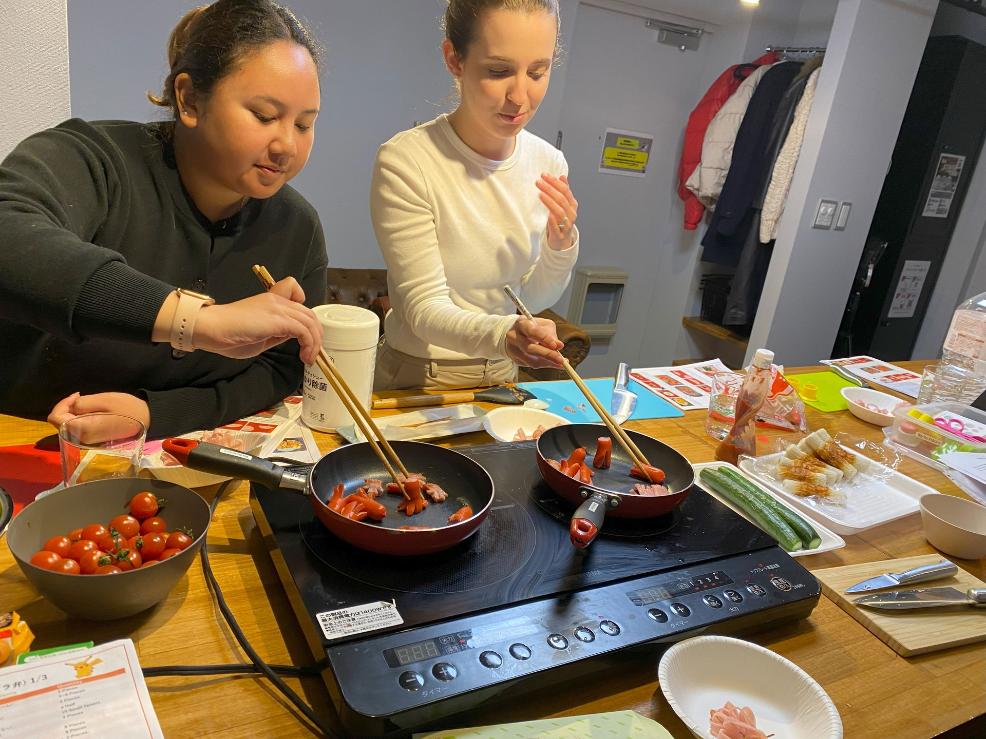 Two guests at a Shinjuku cooking class grilling sausages in a pan.