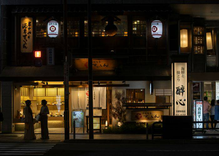 The stylish exteriors of a shop in Kyoto, showing the silhouettes of people talking in the city.