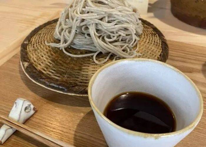 A serving of soba noodles on a serving tray, next to a bowl of dipping broth.