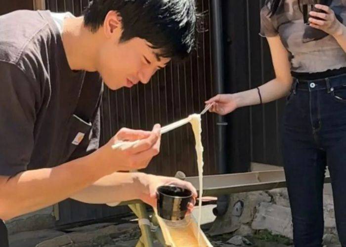 Someone picking up noodles from a nagashi bamboo slide.