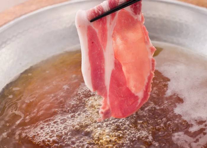 A thin slice of meat being dunked into a boiling broth at Shabushabu Okaka Shinjuku.