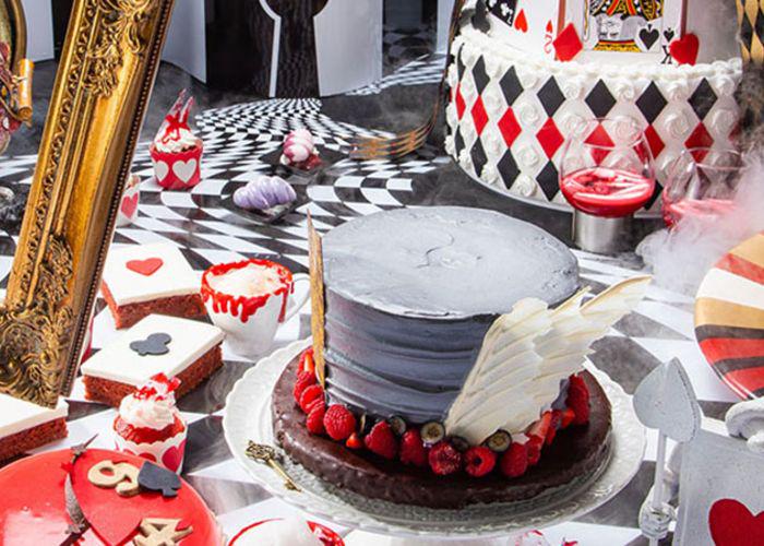 Alice in Wonderland Mad Tea Party-themed buffet with playing cards, red, white, and black checkers, and a cake shaped like the Mad Hatter's hat