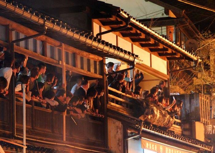 Golden light from the fire illuminates the crowd of people gathered on balconies to watch the Kurama Fire Festival proceeding below