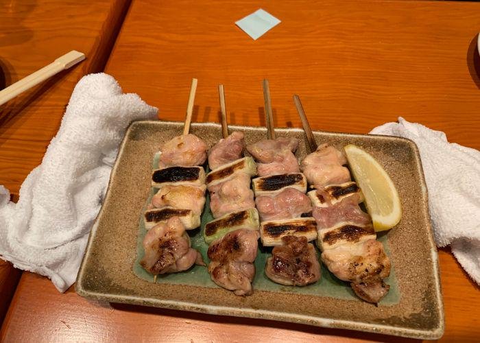 Yakitori skewers on a rectangular plate, with a side of lemon wedge, grilled and charred
