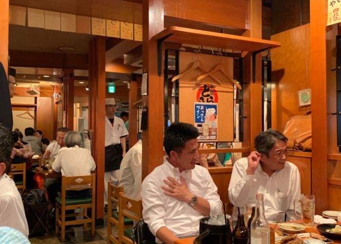 Japanese businessmen wearing white collared shirts sit at an izakaya