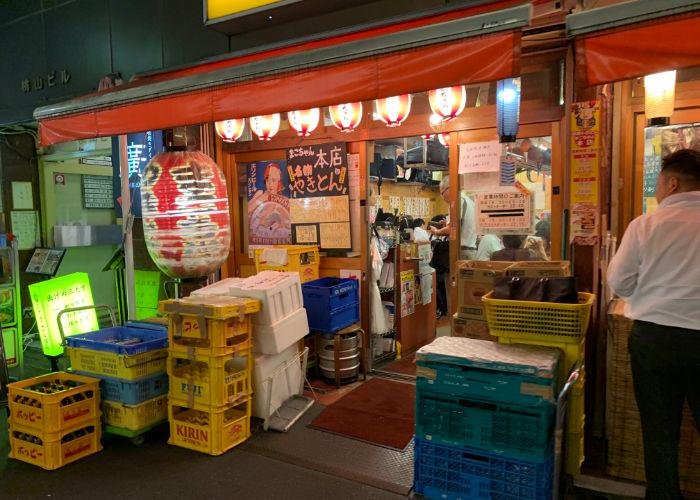 The exterior of a Tokyo izakaya, with red lantern outside, and yellow Kirin boxes stacked outside the door.