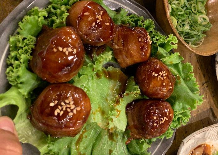 A bed of lettuce upon which several balls of glazed meat, topped with sesame seeds, are resting