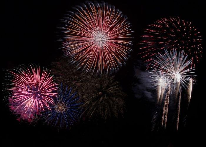 Pink, blue, orange, and white firework bursts in the black sky