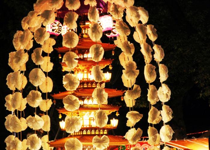 A tall red pagoda towers in the background against a black night sky, lit by lanterns