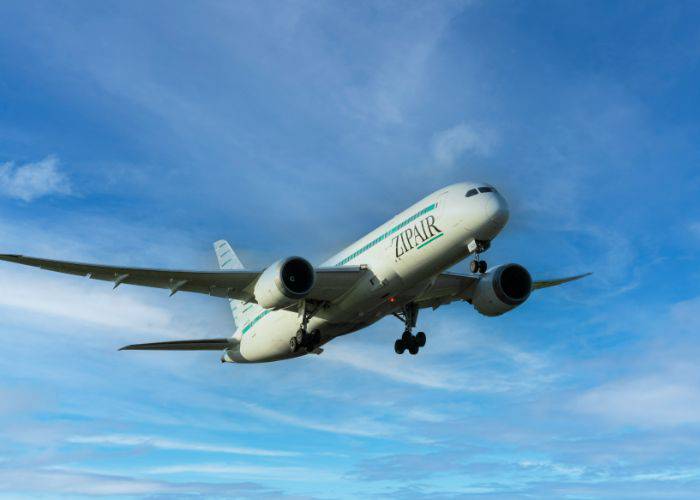 A ZIPAIR plane as seen from below, set against a bright blue sky.