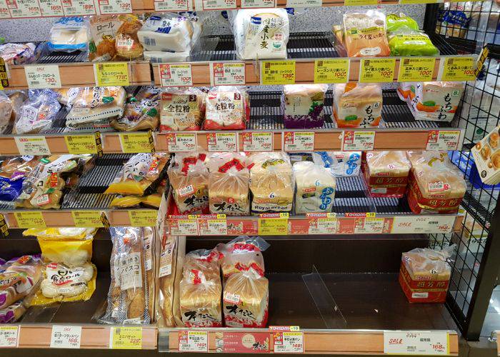 The bread shelves at a Japanese supermarket, featuring many types of bread for purchase.