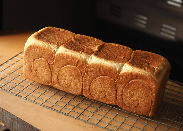 Four fresh loaves of shokupan, cooling on a rack. A swirling pattern is clear on the side.