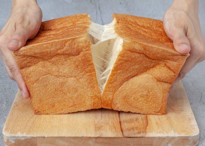 Two hands pulling apart a loaf of Japanese milk bread, showing how fluffy and soft it is inside.