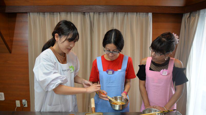 A friendly host is teaching two guests how to cooking Japanese food.