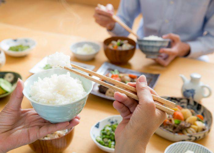 Two people enjoying a traditional Japanese breakfast, using chopsticks to eat from bowls of rice.