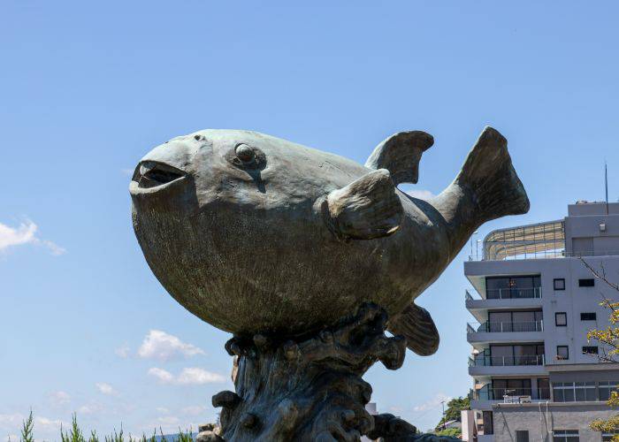 A statue of a puffer fish, set against a blue sky.