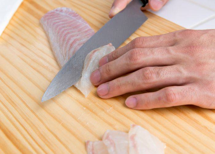 A trained chef with a sharp knife is carefully slicing through fresh fugu puffer fish.