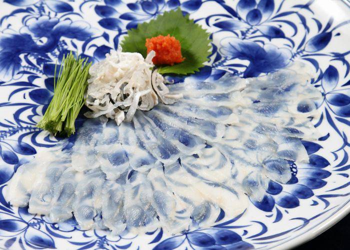 Delicate, thin slices of fugu sashimi, fanned out on an ornamental blue serving plate.