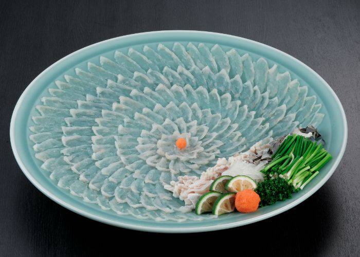 Thin slices of fugu fanned out in a decorative pattern, alongside fresh vegetables and sudachi citrus.