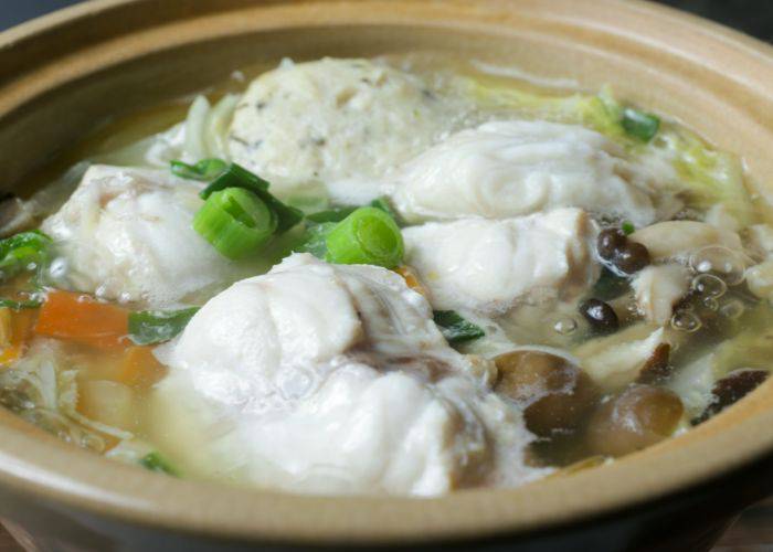 Puffer fish soaking in a hot pot broth with fresh vegetables.