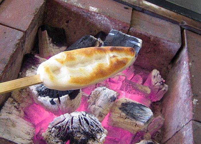 A Miyagi white fish cake on a stick cooking over a charcoal fire