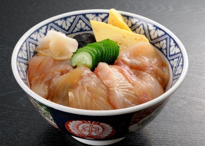 A bowl of Sendai zuke-don which is raw white fish with cucumbers in the middle on a bed of rice