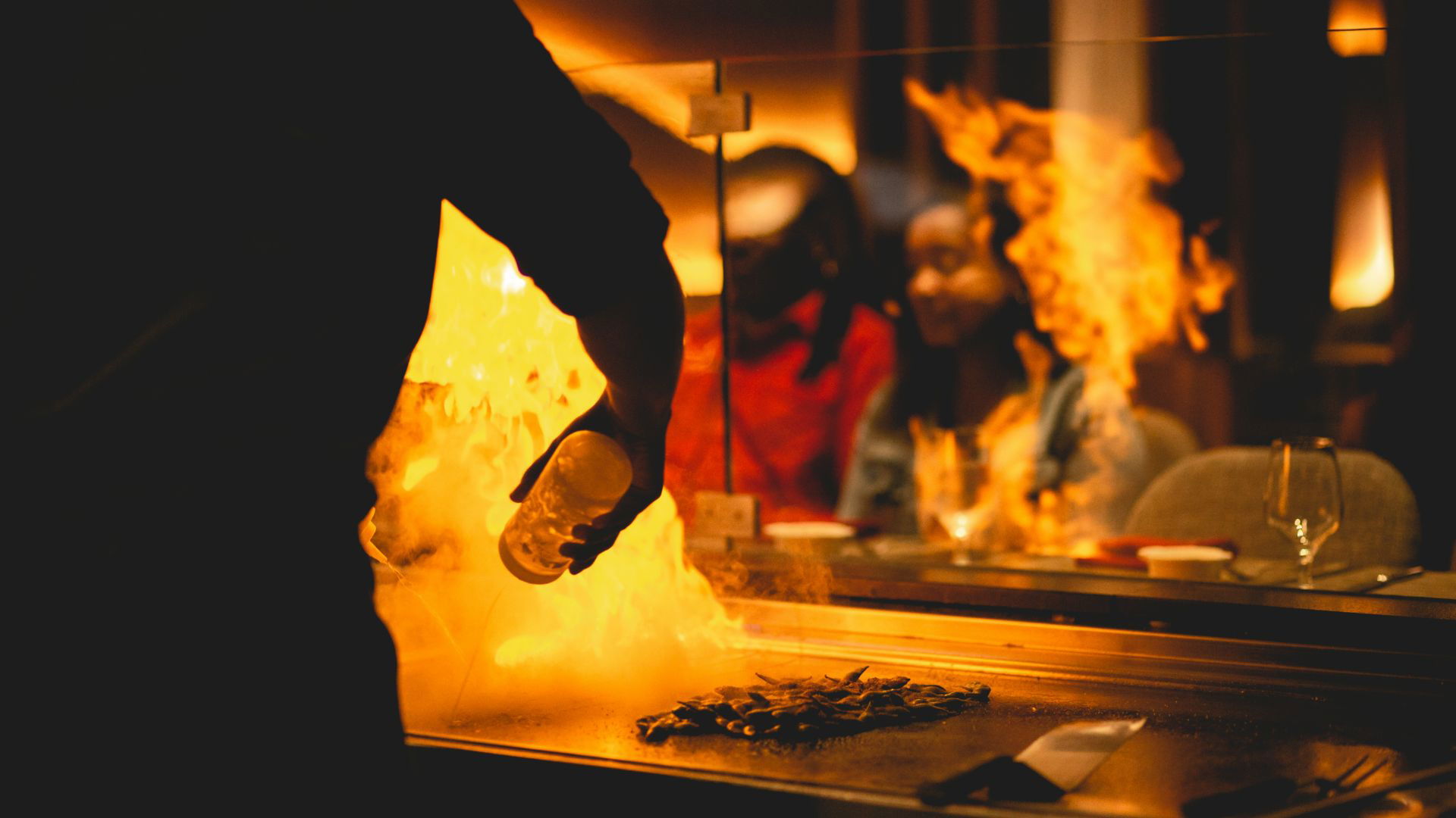 Chef preparing flaming dish at teppanyaki grill with onlookers