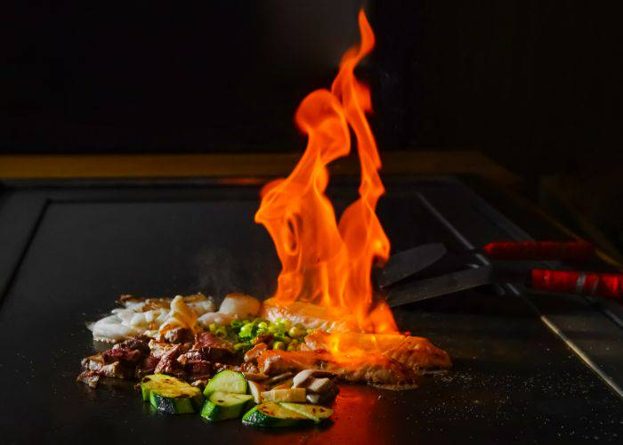 A teppanyaki grill with a high flame, grilling meats and vegetables.