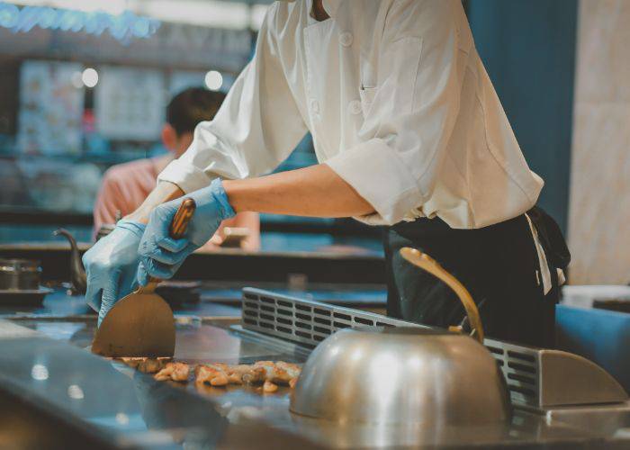 A chef in blue gloves cooking ingredients on a teppanyaki grill.