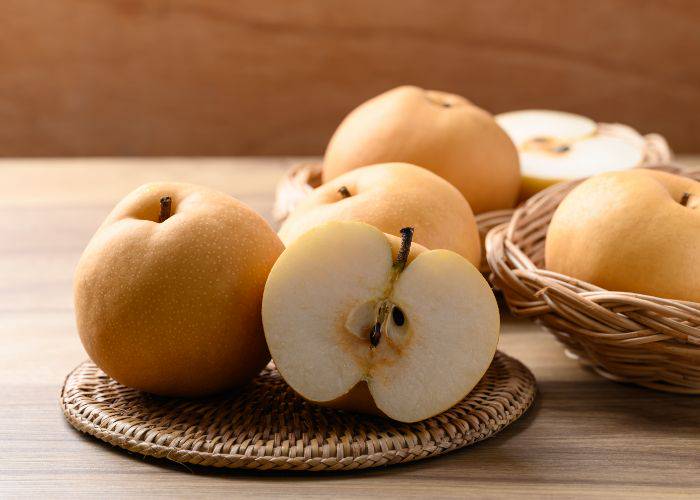 A few Asian pears on a mat, one of which is cut in half.