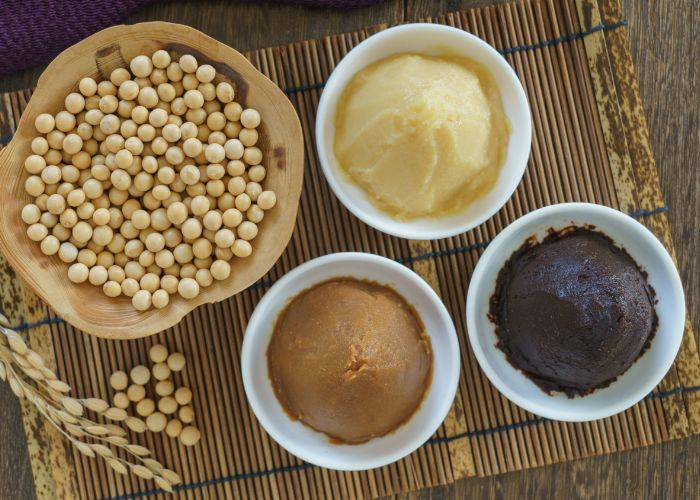 Three bowls of miso paste: white, red and mixed. Next to a bowl of soybeans.