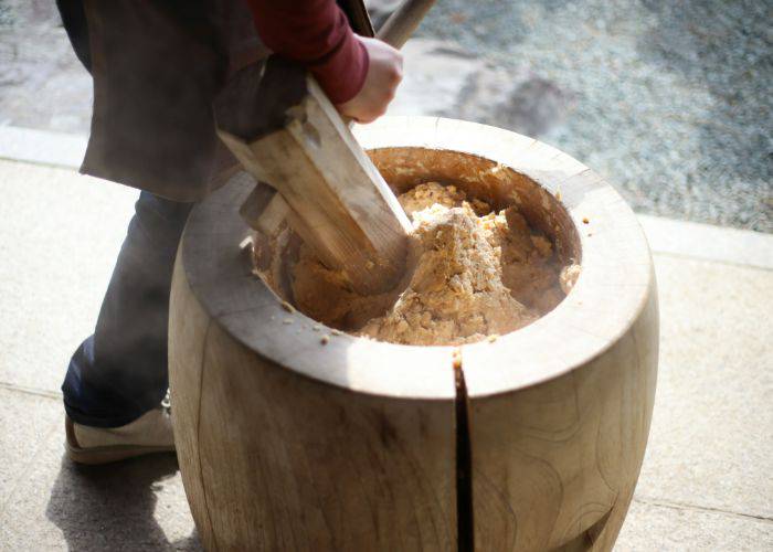 Someone using a traditional tool to mash soybeans into miso paste.