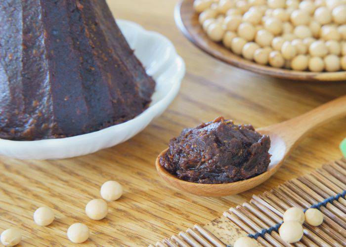 A wooden spoon with red miso, next to a towering pile of red miso paste.