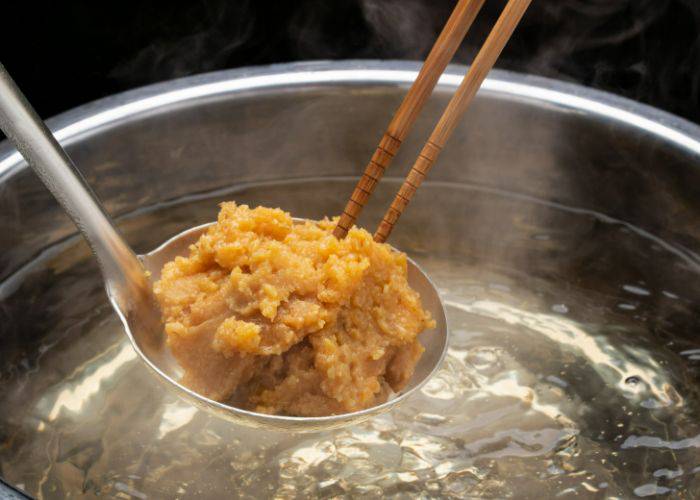 A spoonful of mixed miso on a spoon above boiling water, about to be mixed in for miso soup.