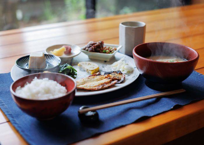 A picturesque traditional Japanese breakfast, complete with grilled fish, steamed rice, miso soup, pickled veggies and more.