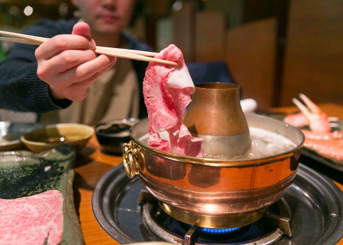 A man with chopsticks dipping a piece of raw kobe beef into a shabu shabu 