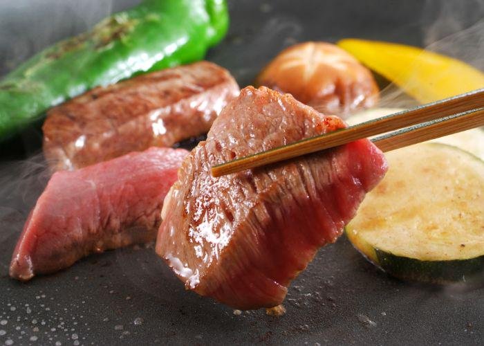 A pair of chopsticks holding a piece of cooked Kobe beefsteak 