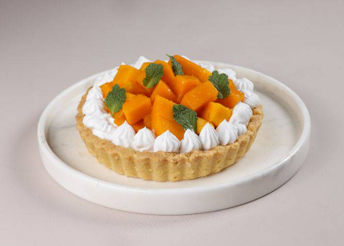 A vibrant fruit tart, featuring fresh mango in the center of a short crust pastry and whipped cream.