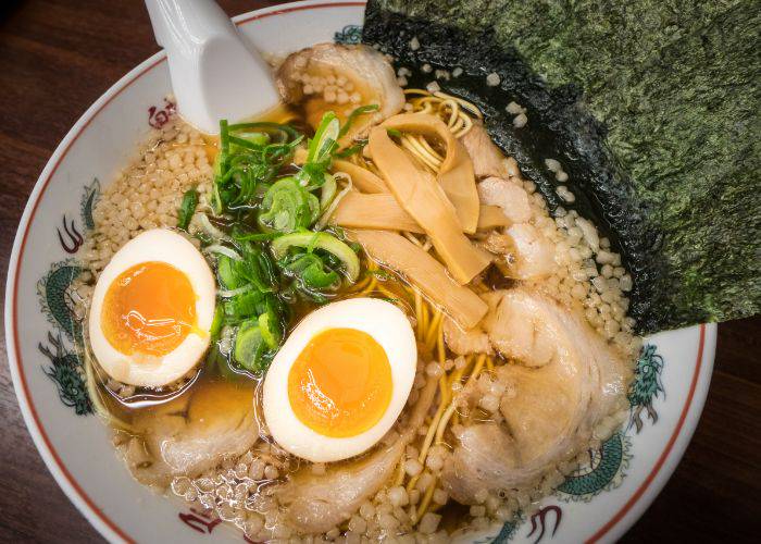 A bowl of ramen featuring noodles, a soft-boiled egg, meat, spring onions and slices of bamboo shoot.