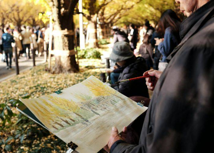 A person painting the golden yellow of gingko trees in front of them.