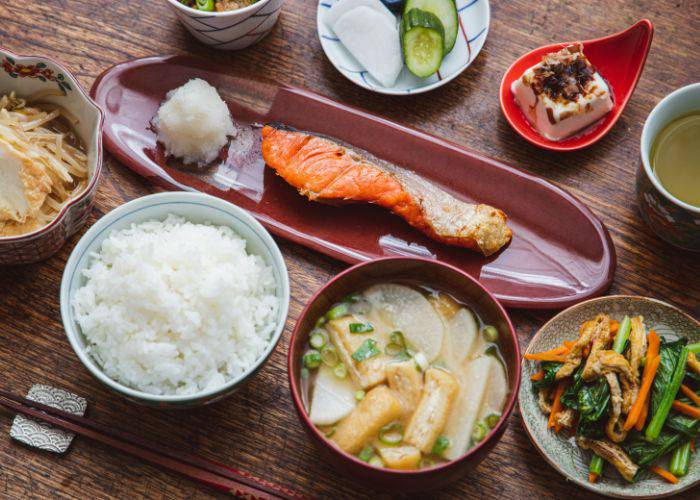 A traditional set meal in Japan, including grilled salmon, rice bowl, tofu, miso soup, pickles and more.