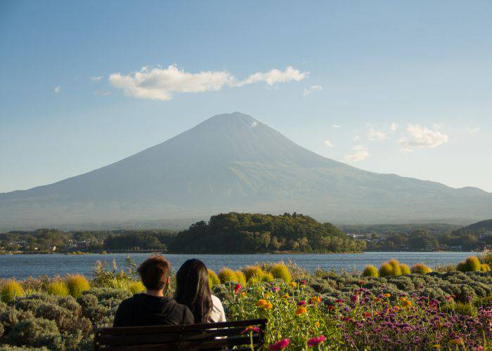 A couple sitting on a bench, looking out over a lake and mountain.