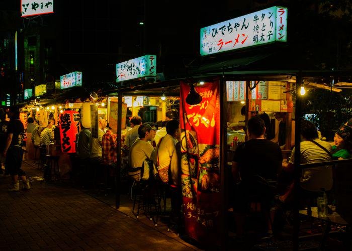 A crowd of people sat at street food stalls at night 