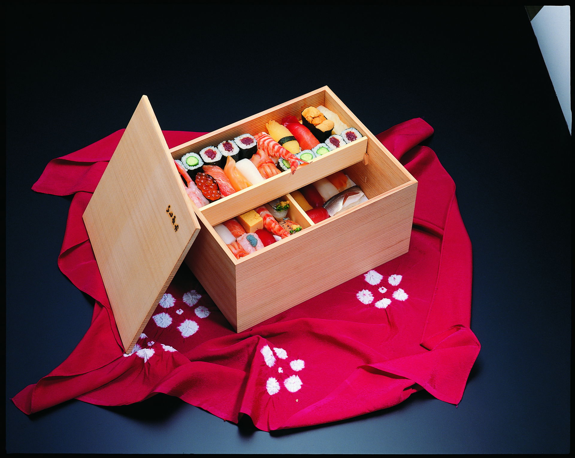 A deep wooden serving box of different sushi types, including nigiri and maki, at Sushi Ishikawa.