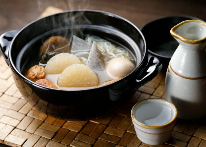 A steaming bowl of Kanazawa oden, served alongside a cup of sake.